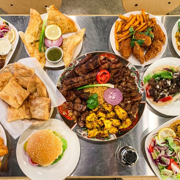 Abundant spread of diverse restaurant dishes, including grilled meats, rice, salads, fried chicken, and a burger.