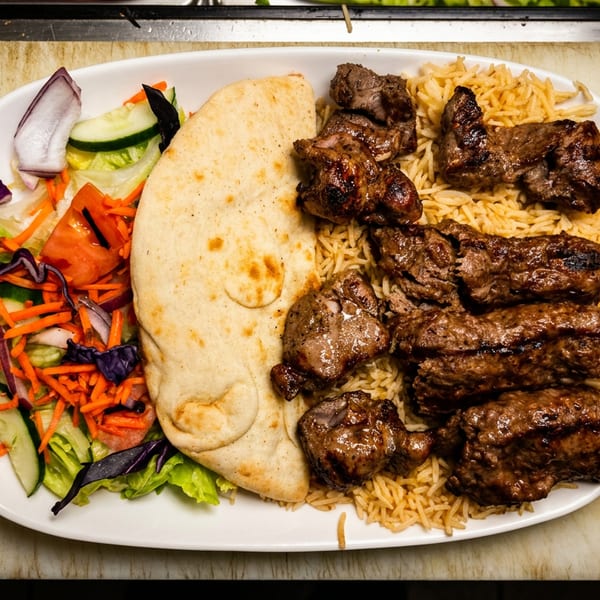 Grilled meat kebabs, rice, flatbread, and fresh salad on a white plate.