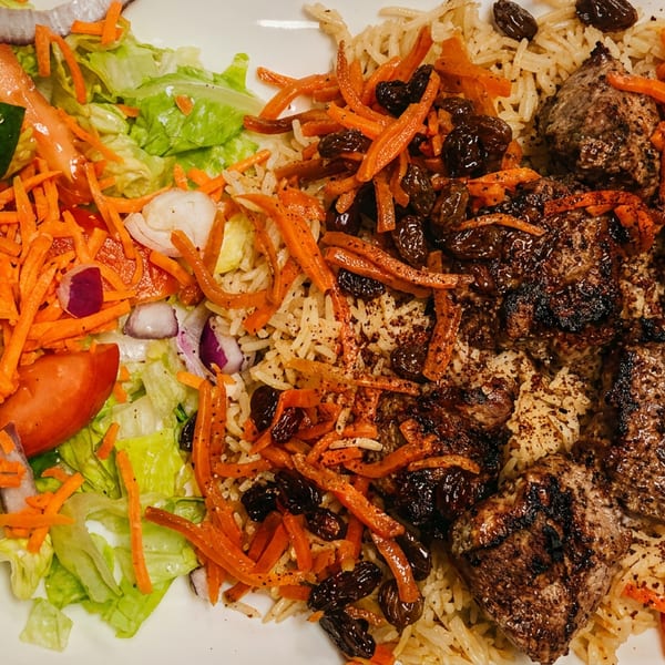 Plate of rice with meat, shredded carrots, and raisins, served with a fresh side salad.