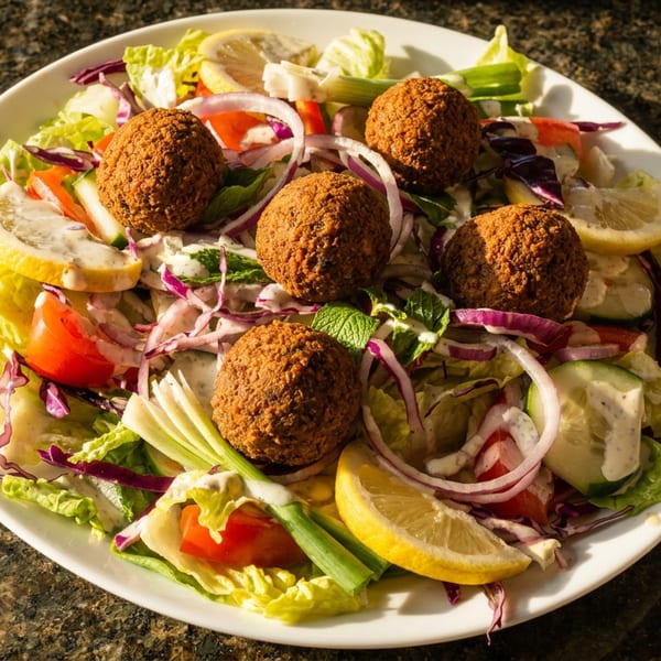A colorful falafel salad with mixed greens, red onion, tomato, cucumber, lemon, and a creamy dressing.