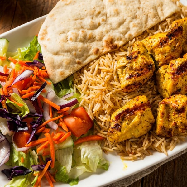 Plate of grilled chicken skewers, basmati rice, fresh garden salad, and pita bread.